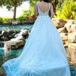 Bride in an ivory white long gown, posing with her back to the camera in front of a water pool surrounded by trees